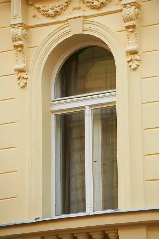 Bílá špaletová okna s obloukovým záklenkem ve žluté fasádě