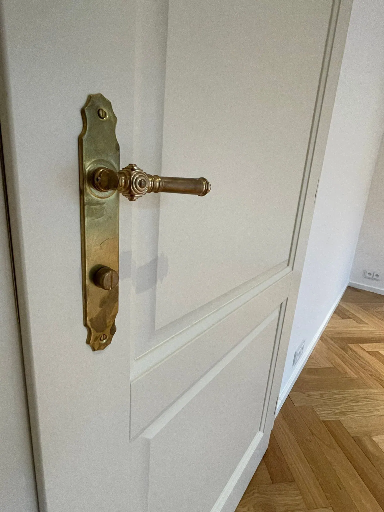Bílé dveře s mosaznou klikou a parketová podlaha