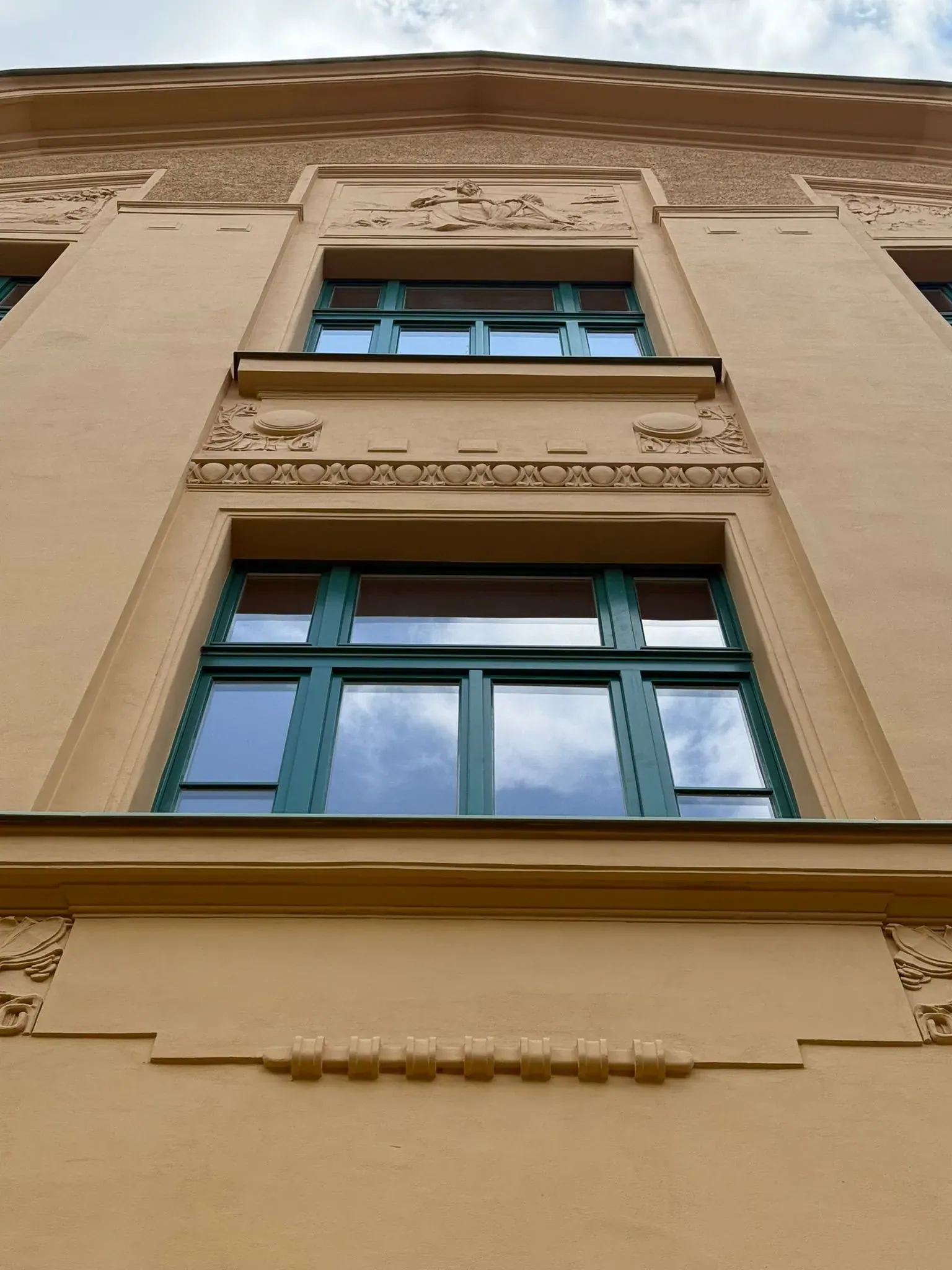 Zelená špaletová okna na historické žluté fasádě