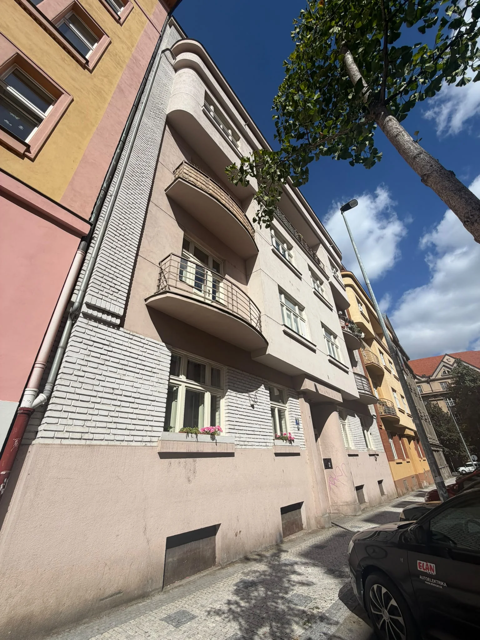 Uliční fasáda se světlými okny a balkony při pohledu podél chodníku, Kyjevská 779/9, Praha 6.