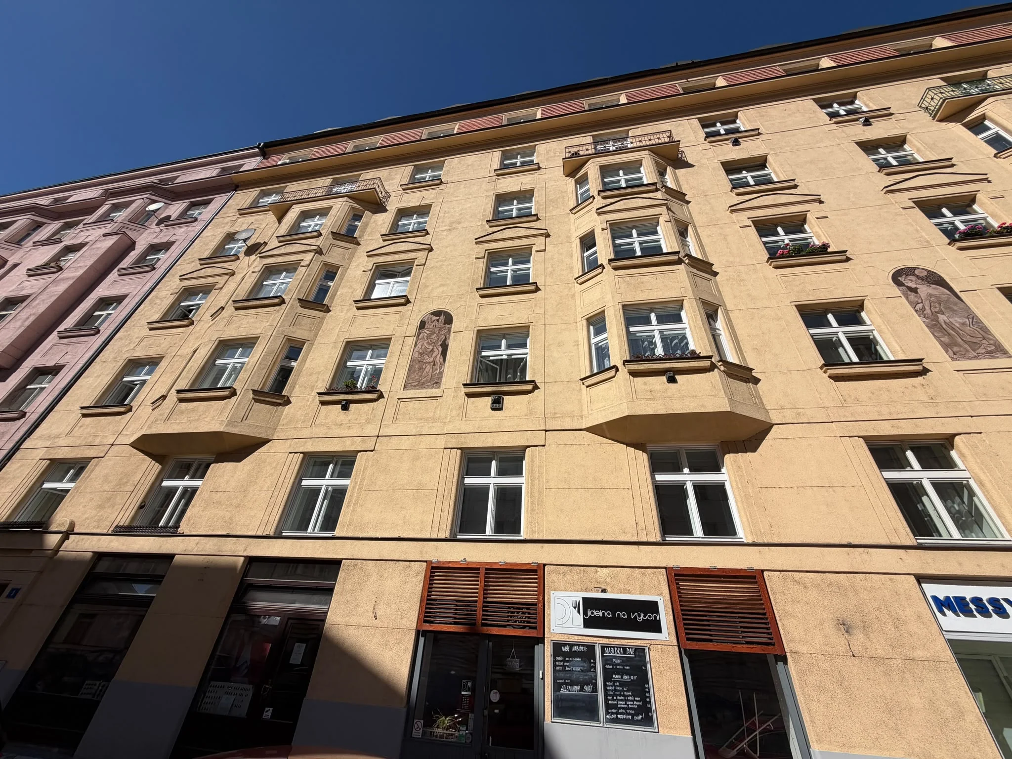 Pohled zespodu na špaletová okna a arkýře ve žlutém průčelí domu Ladova 2044/3 v Praze 2.